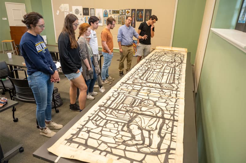 Professor Stephen Hartley and students examine the full-scale cartoon of the Protestant Stream of Christianity window designed by Charles Z. Lawrence for the National Cathedral in Washington DC. 